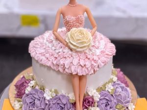 Purple Rosette Doll Cake in Lahore — A doll cake with a two-tone gown — pale pink rosettes above, deep purple roses below — and a sugar rose held i