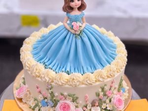 Blue Gown Doll Cake in Lahore — A doll cake with a pleated sky-blue gown, sugar roses and blossom trailing around the base and an ivory bodice