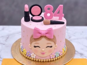 Pink Doll Face Makeup Cake in Lahore — A blush pink cake with a doll face and bow piped on the front, a large glitter number on top and a small set o