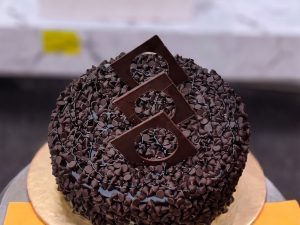 Chocolate Chip Fudge Cake in Lahore — A chocolate fudge cake covered in chocolate chips with a large chocolate shard standing on top — a simple, dee