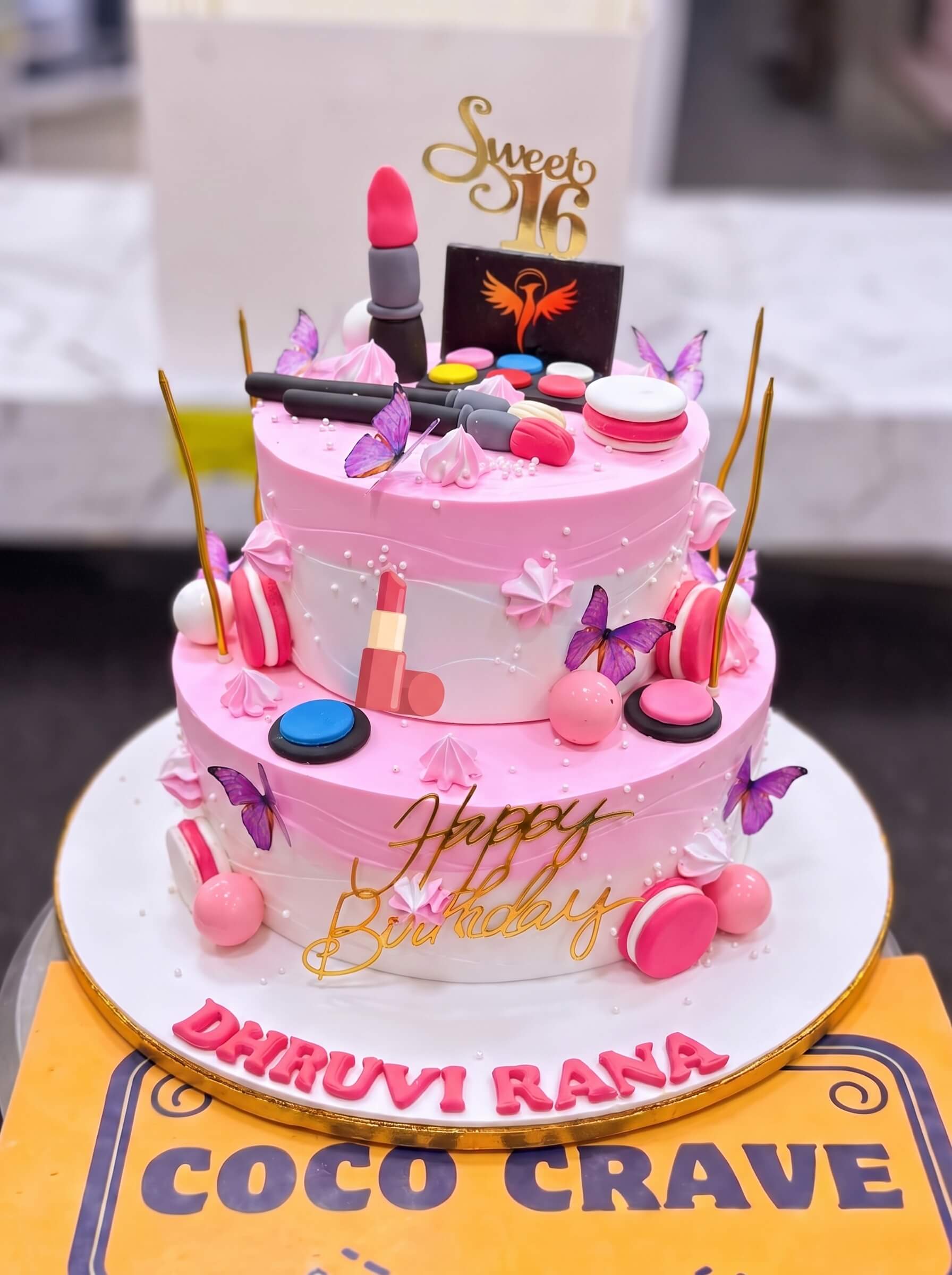 Two Tier Barbie Makeup Cake in Lahore — Coco Crave Lahore Two Tier Barbie Makeup Cake in Lahore — A two tier pink makeup cake — a white lower tier with a piped name, a pink upper tier with butterflies, lipsti