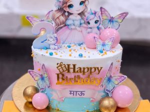 Doll and Butterfly Birthday Cake in Lahore — A pastel blue and white cake with a printed doll cutout standing at the back, butterflies on wires and gold pe