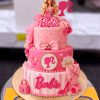 Barbie Logo Two Tier Cake in Lahore 1 Barbie Logo Two Tier Cake in Lahore — A hot pink two tier Barbie cake with the Barbie script, a doll silhouette medallion, a fondant handbag, bow an