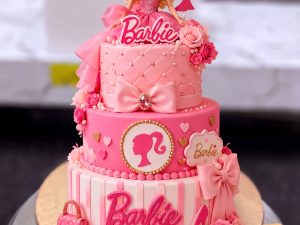 Barbie Logo Two Tier Cake in Lahore — A hot pink two tier Barbie cake with the Barbie script, a doll silhouette medallion, a fondant handbag, bow an