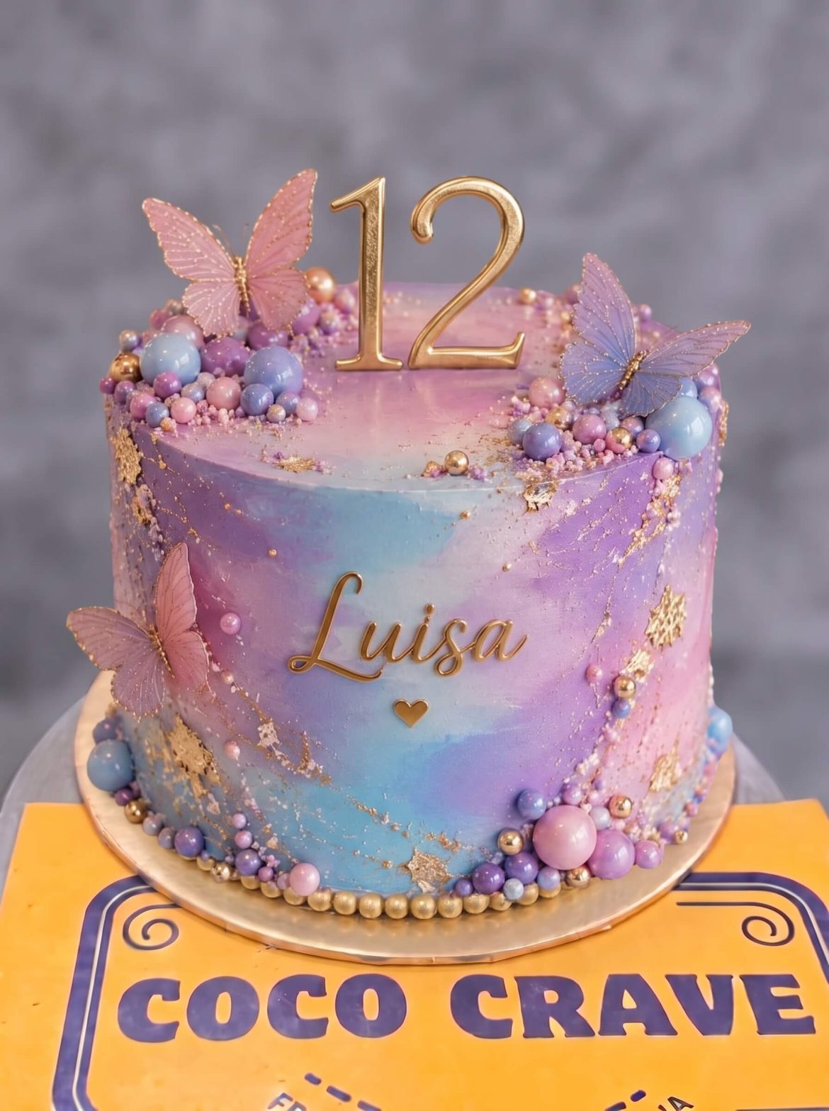 Barbie Butterfly Galaxy Cake in Lahore — A pastel watercolour cake washed in pink, lilac and blue, with 3D butterflies climbing the side, a gold name a