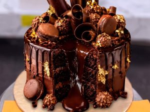 Chocolate Macaron Drip Cake in Lahore — A chocolate drip cake crowned with macarons, chocolate cigar curls, truffles and edible gold leaf — an elegant