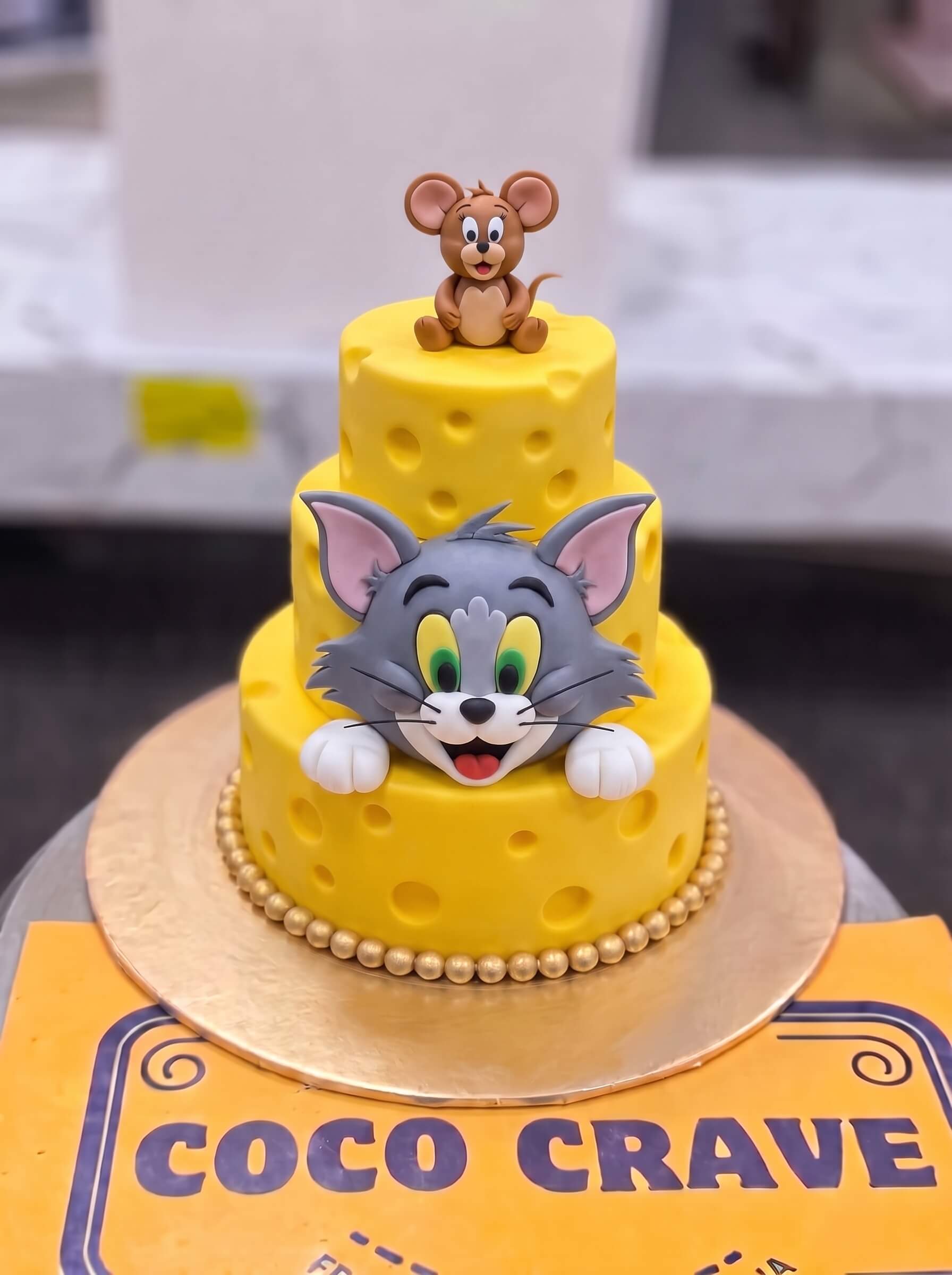 Tom and Jerry Cheese Cake in Lahore — CocoCrave.pk Tom and Jerry Cheese Cake in Lahore by CocoCrave.pk — two tier Tom and Jerry cheese cake in yellow and grey