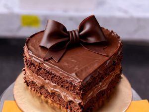 Chocolate Bow Heart Cake in Lahore — A heart-shaped chocolate cake topped with a large handmade chocolate bow over exposed fudge layers — a gift-st