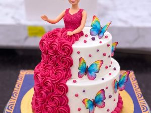 Two Tier Barbie Butterfly Cake in Lahore — A two tier Barbie cake — a magenta rosette tier below, a white tier scattered with printed butterflies above,