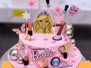 Barbie Makeup Theme Cake in Lahore — A pink Barbie makeup cake loaded with fondant lipsticks, brushes, nail polish and a Barbie face plaque — the g