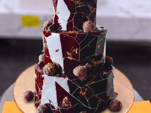 Two Tier Chocolate Marble Cake in Lahore — A two tier chocolate cake with a black, burgundy and gold marbled finish topped with truffles and berries — a