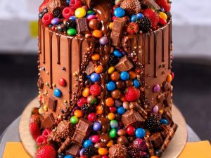 Chocolate Overload Loaded Cake in Lahore — A tall chocolate overload cake loaded with KitKat fingers, a tipping Nutella jar, gems, chocolate bars and fre