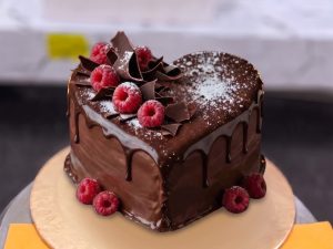 Chocolate Raspberry Heart Cake in Lahore — A heart-shaped chocolate drip cake with fresh raspberries, chocolate shards and a dusting of icing sugar — a c