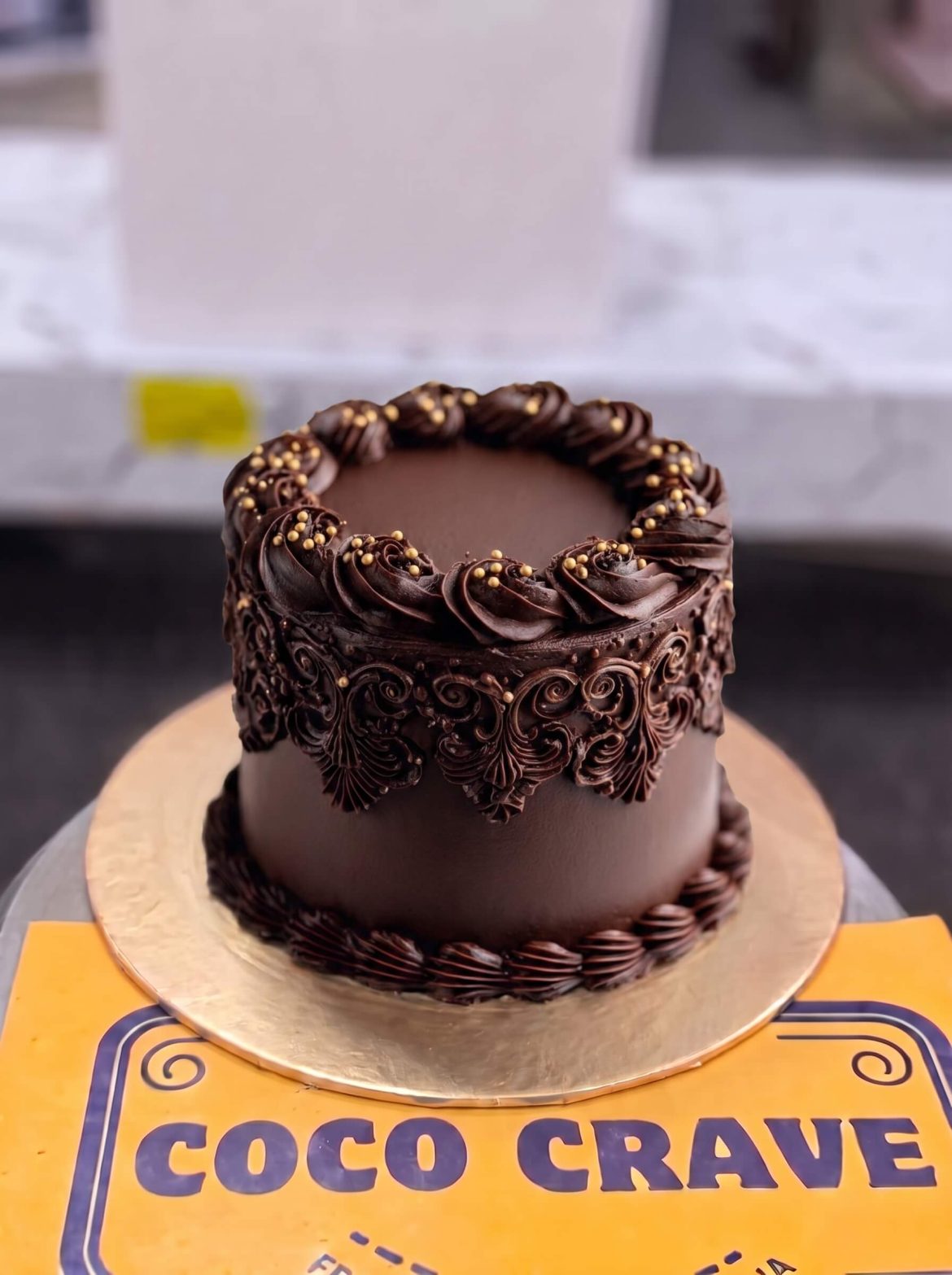 Chocolate Ganache Celebration Cake in Lahore — A smooth dark chocolate ganache cake finished with hand-piped scrollwork around the sides — our most classic c