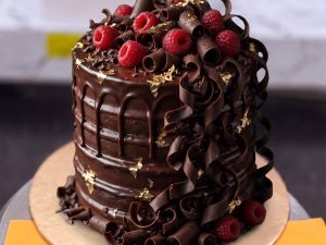 Chocolate Curls and Raspberry Cake in Lahore — A dark chocolate cake covered in hand-rolled chocolate curls with fresh raspberries and gold flecks on top — a