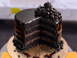 Chocolate Mirror Glaze Cake in Lahore — A tall chocolate cake under a glossy mirror glaze with six visible fudge layers inside and a piped chocolate c