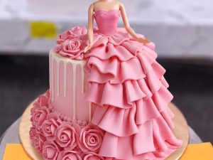 Pink Rose Gown Doll Cake in Lahore — A doll cake with a deep pink gown built from layered ruffles and piped roses cascading down one side. A classi