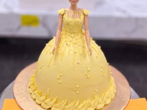 Yellow Gown Princess Doll Cake in Lahore — A doll cake in a golden yellow gown with a scalloped hem and a gold-sparkle bodice — a Belle-style princess do