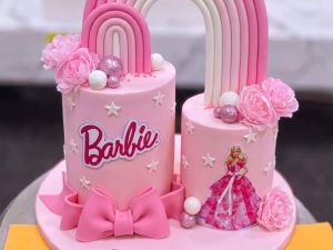 Barbie Rainbow Arch Cake in Lahore — A pink Barbie cake with a tall pink rainbow arch rising between two tiers, a fondant bow, roses and the Barbie