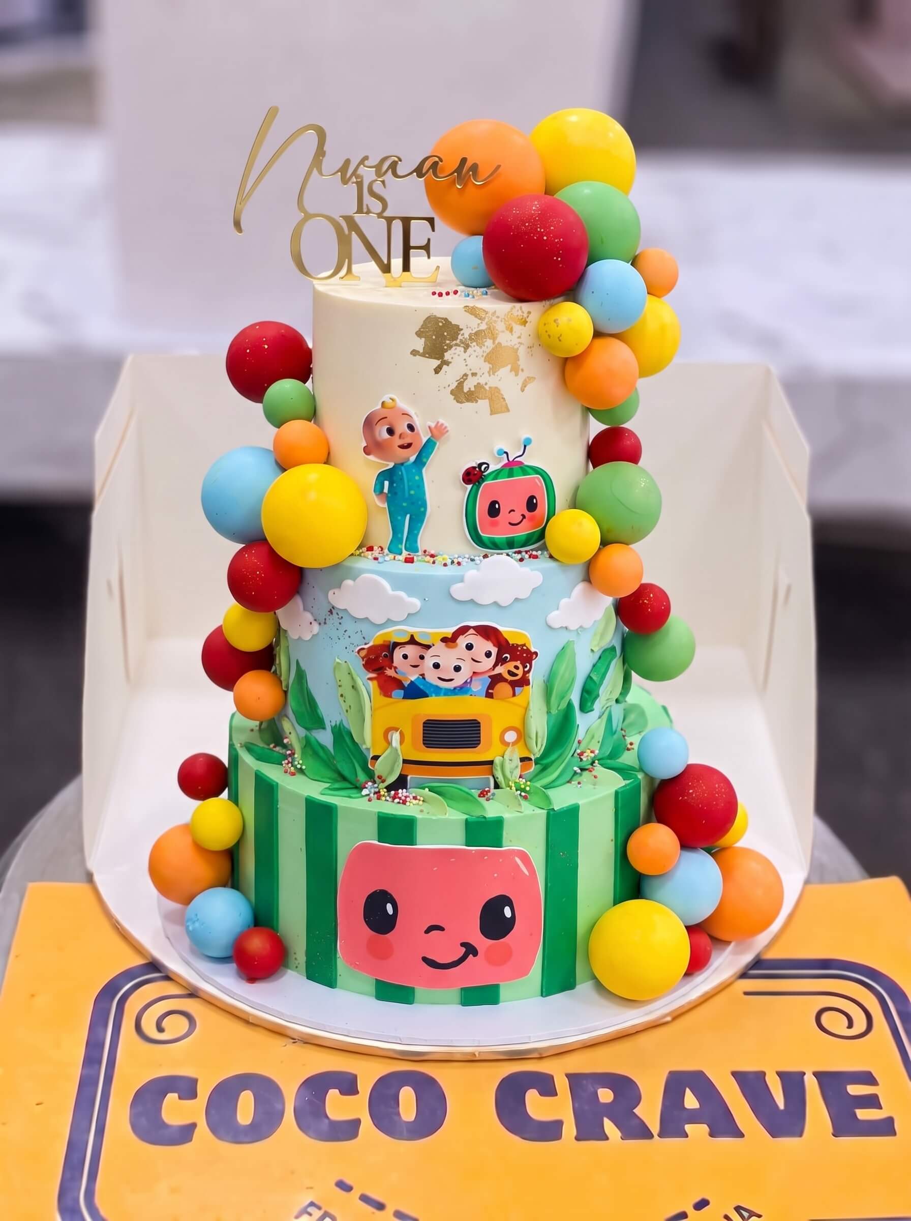 Cocomelon First Birthday Cake in Lahore — CocoCrave.pk Cocomelon First Birthday Cake in Lahore by CocoCrave.pk — three tier Cocomelon first birthday cake in white, blue and green